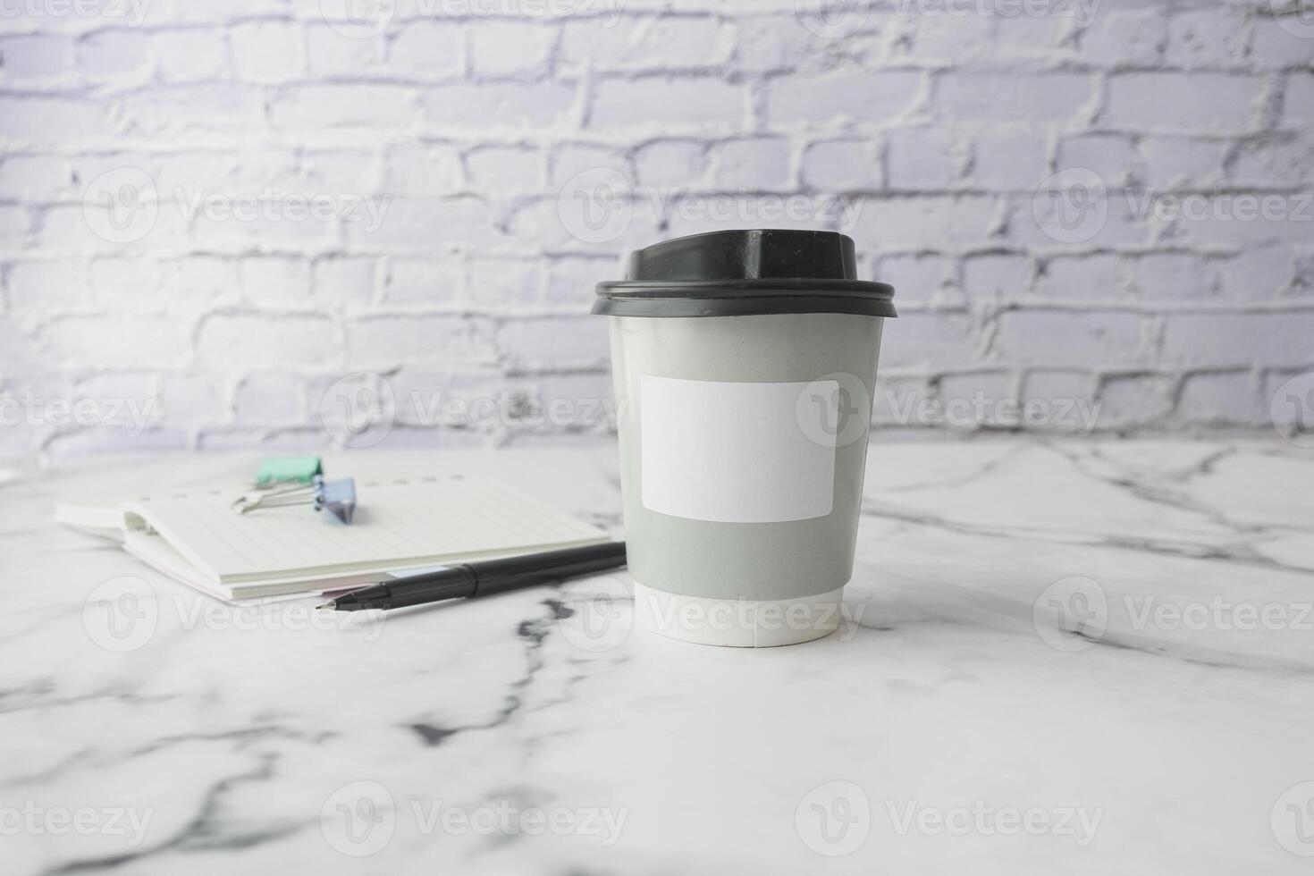 A disposable coffee cup is placed on a marble surface next to a notebook and pen photo