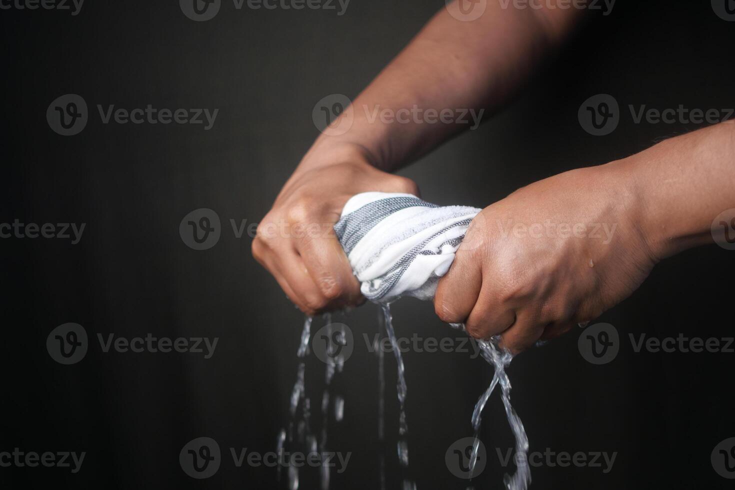 Hands squeeze wet towel against black background. draining water from wet towel.. photo
