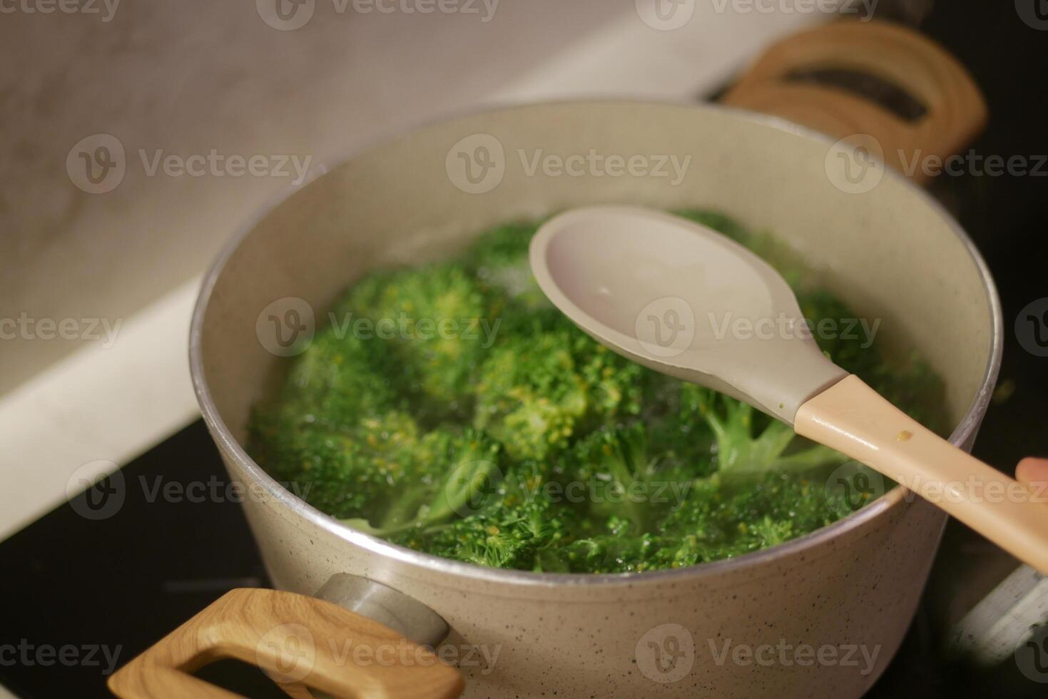 Boiling broccoli in a pot with a wooden spoon on the stove, preparing a healthy meal photo