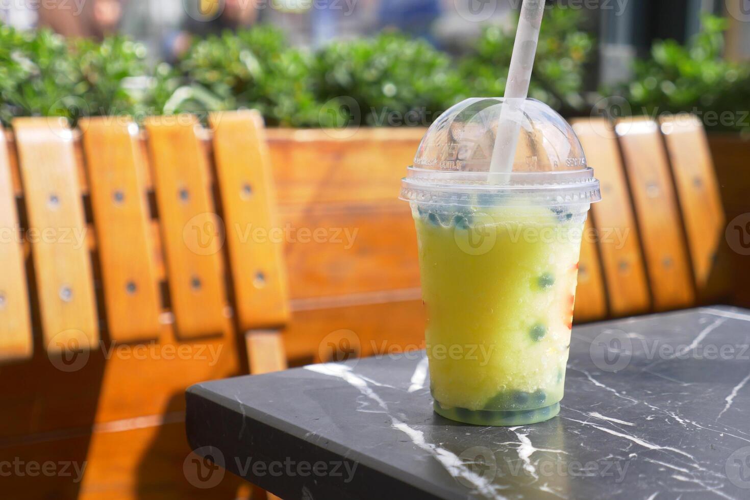Refreshing yellow bubble tea with tapioca pearls sits on a marble table outside a cafe, photo