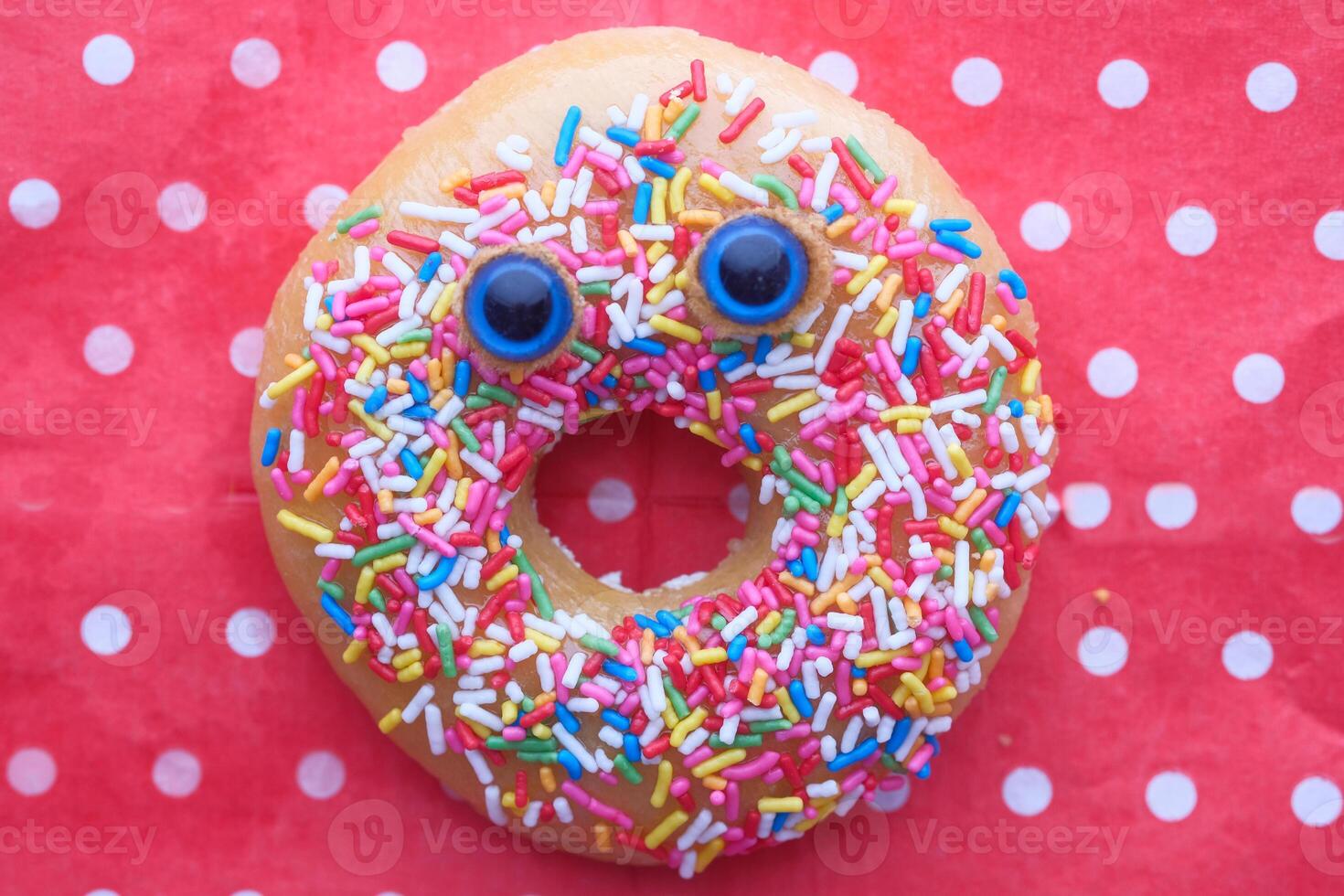 Funny smiling face donut with sprinkles on red background. photo