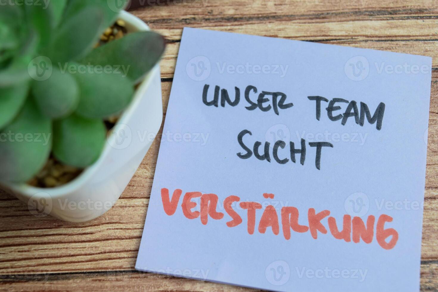 Concept of Learning language - German. Unser Team Sucht Vestarkung it means Our team is looking for reinforcements written on sticky notes. German language isolated on Wooden Table. photo