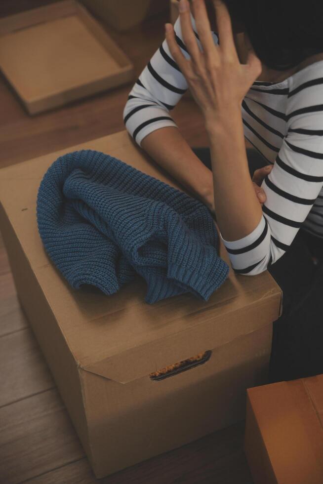 Two Asian blogger showing clothes in front of the camera to recording vlog live streaming at her shop. Online Shopping Cart notion. on sofa at home photo