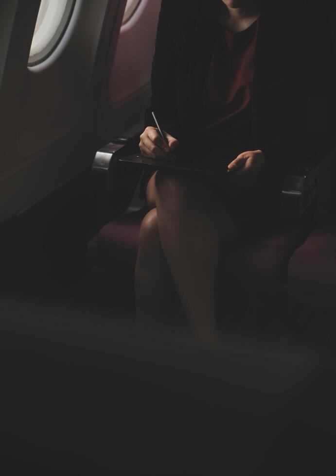 Blonde female tourist checking incoming notification on smartphone sitting on seat of airplane with netbook.Young businesswoman share media from telephone on laptop computer during plane flight photo