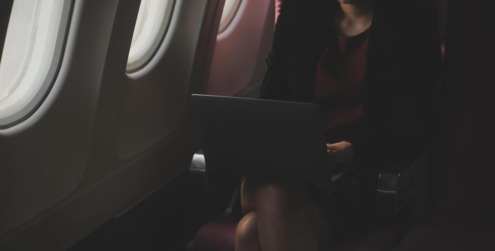 Blonde female tourist checking incoming notification on smartphone sitting on seat of airplane with netbook.Young businesswoman share media from telephone on laptop computer during plane flight photo