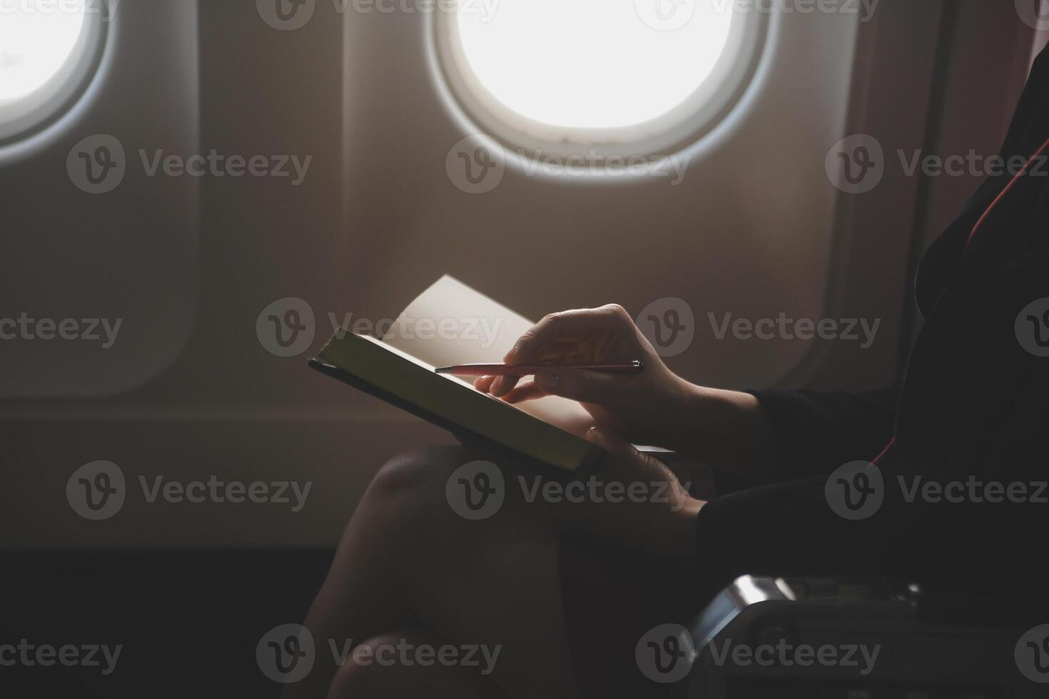 Blonde female tourist checking incoming notification on smartphone sitting on seat of airplane with netbook.Young businesswoman share media from telephone on laptop computer during plane flight photo