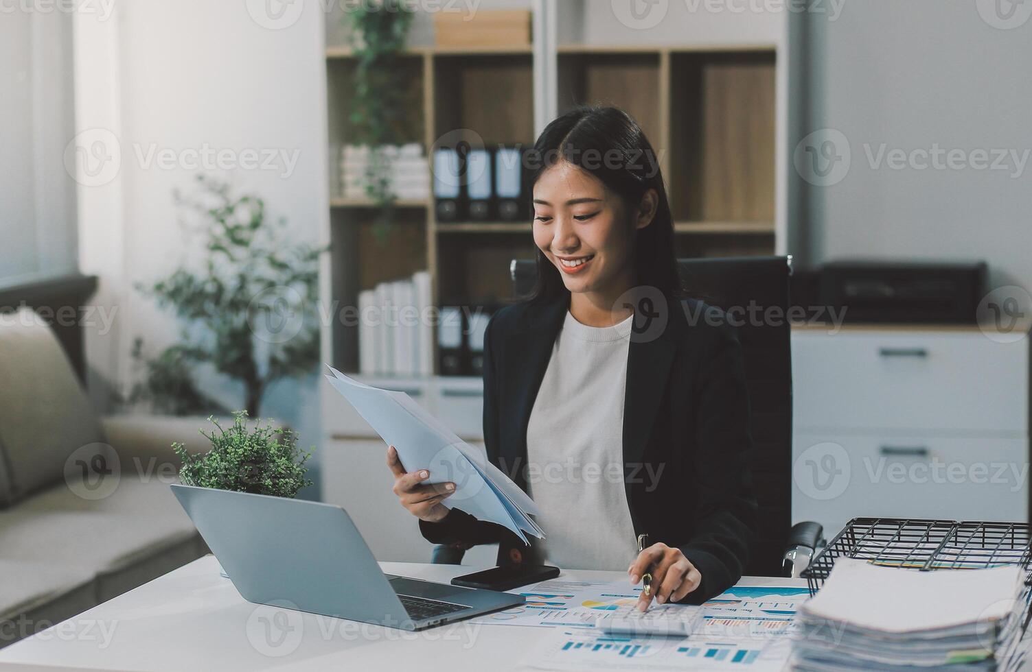 Confident millennial indian female business analyst financial advisor preparing statistic report studying documents on work desk, browsing information online using pc, writing out notes on paper sheet photo