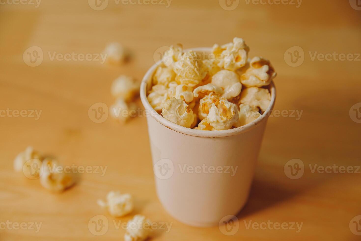 A bucket of popcorn, top-view, warm colors, light brown wooden background, flat lay, daylight macro close-up photo