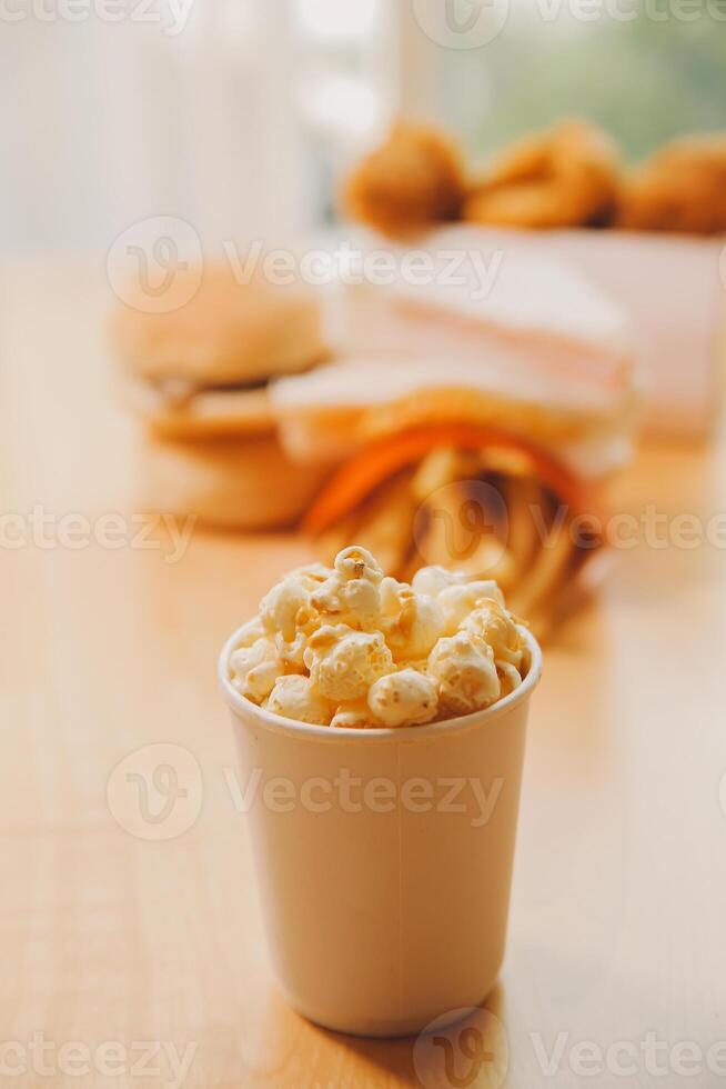 A bucket of popcorn, top-view, warm colors, light brown wooden background, flat lay, daylight macro close-up photo