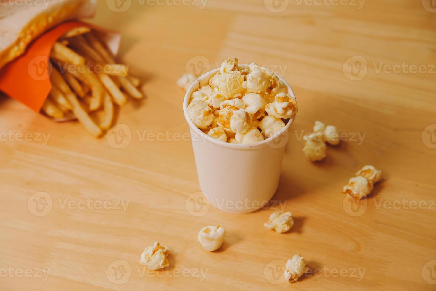 A bucket of popcorn, top-view, warm colors, light brown wooden background, flat lay, daylight macro close-up photo