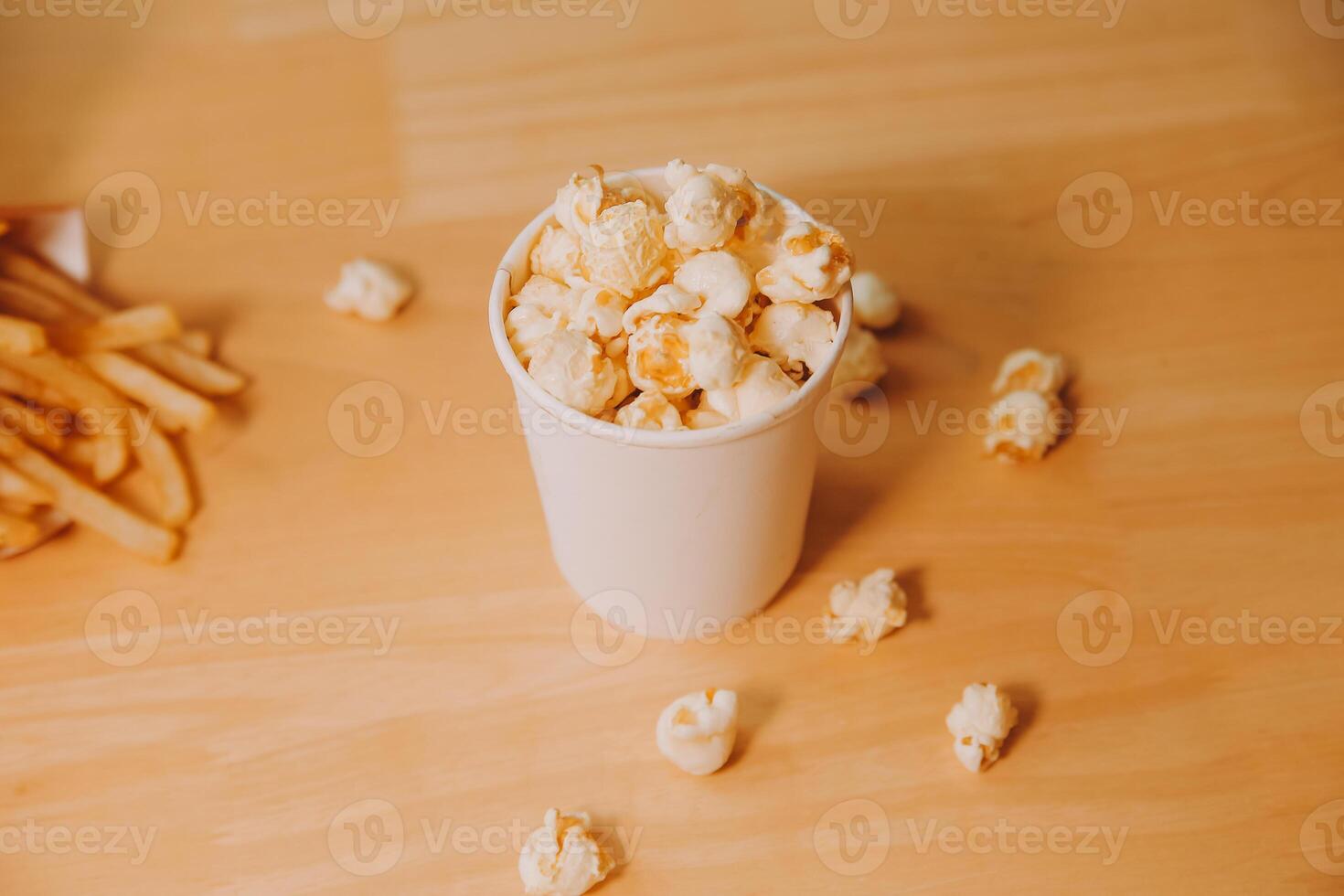 A bucket of popcorn, top-view, warm colors, light brown wooden background, flat lay, daylight macro close-up photo