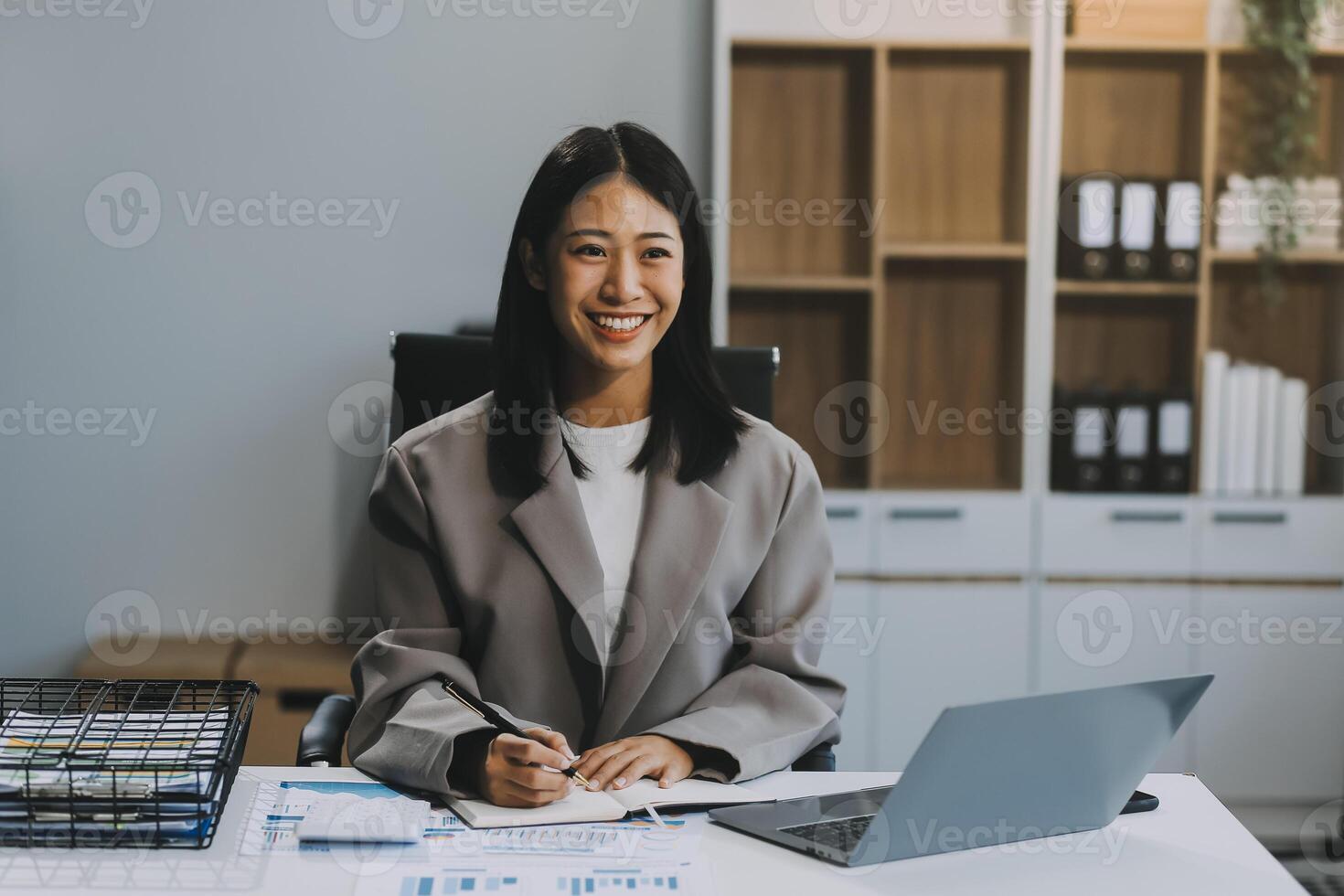 Confident millennial indian female business analyst financial advisor preparing statistic report studying documents on work desk, browsing information online using pc, writing out notes on paper sheet photo