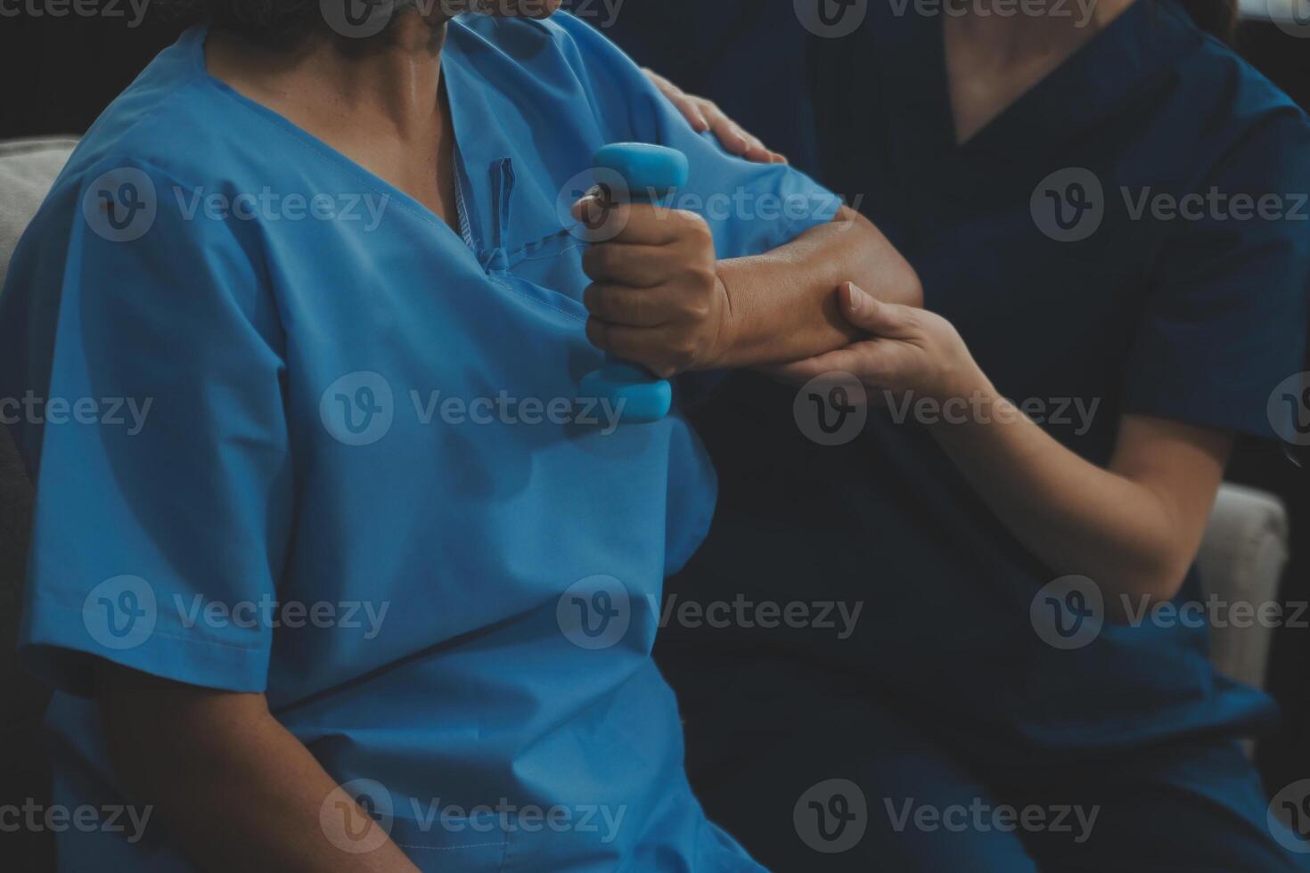 Old woman training with physiotherapist using dumbbells at home. Therapist assisting senior woman with exercises in nursing home. Elderly patient using dumbbells with outstretched arms. photo