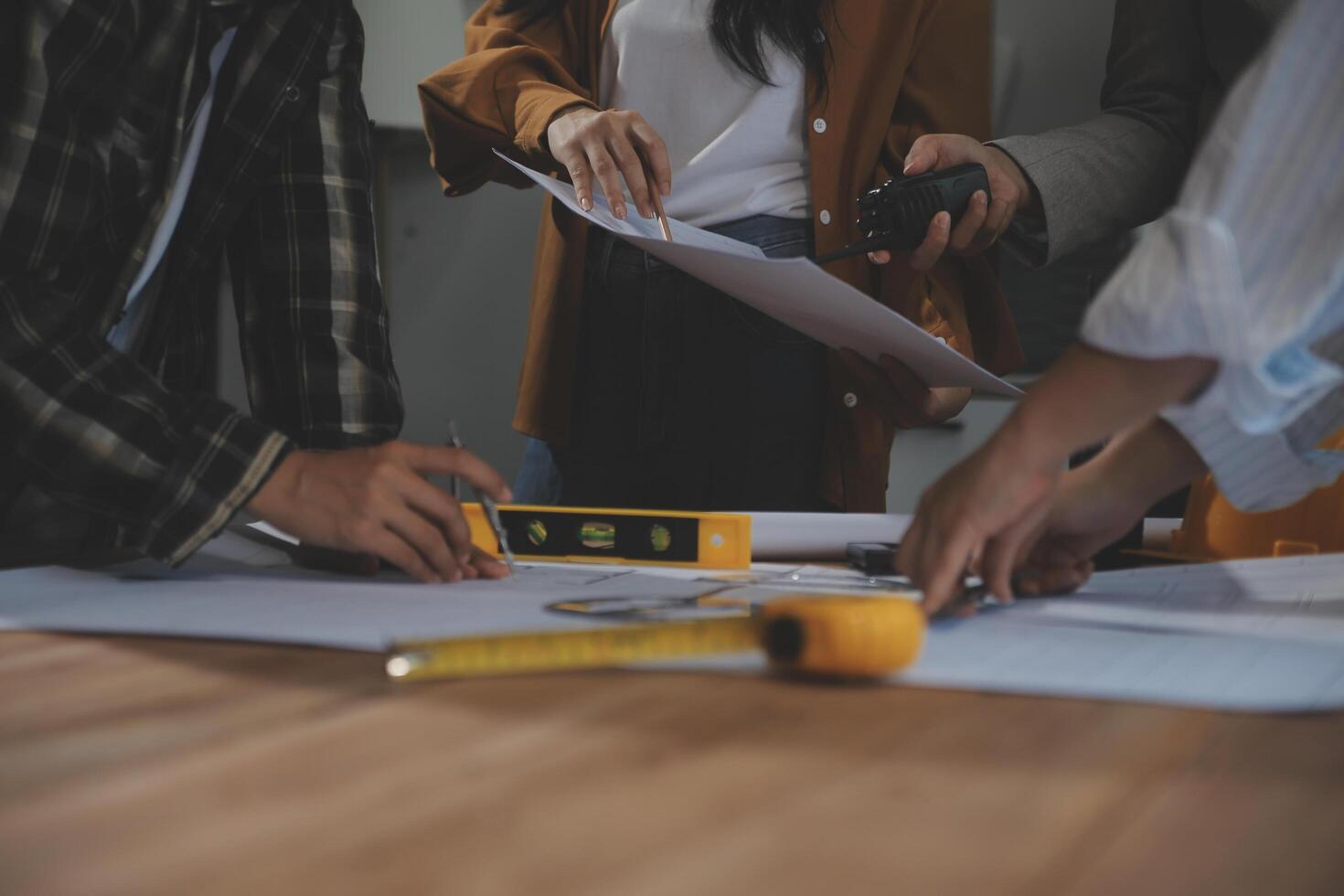 Team of multiethnic architects working on construction plans in meeting room. Engineers discussing on project in office. Mature businessman and woman standing around table working on blueprint. photo