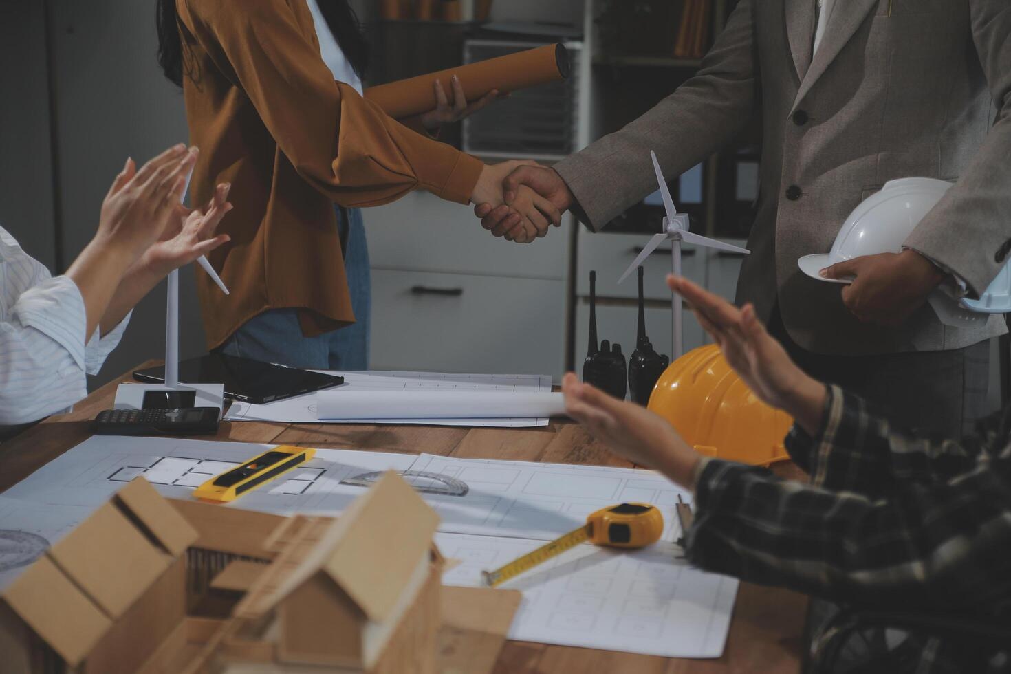 Construction team shake hands greeting start new project plan behind yellow helmet on desk in office center to consults about their building project. in sun light photo