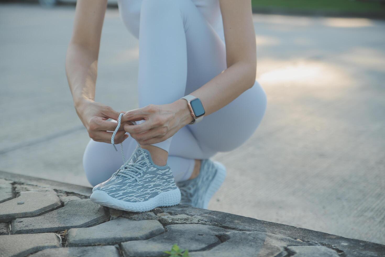 Mature fitness woman tie shoelaces on road. Cheerful runner sitting on floor on city streets with mobile and earphones wearing sport shoes. Active latin woman tying shoe lace before running. photo