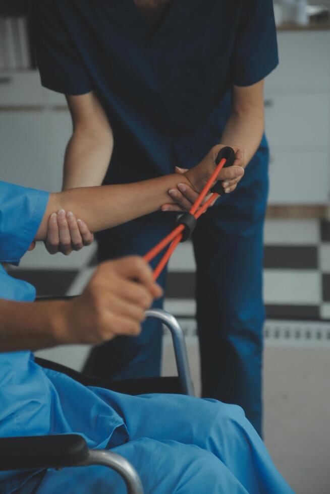 Personal trainer assisting senior woman with resistance band. Rehabilitation physiotherapy worker helping old patient at nursing home. Old woman with stretch band being coached by physiotherapist. photo