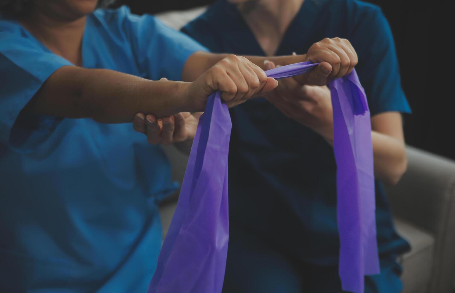 Personal trainer assisting senior woman with resistance band. Rehabilitation physiotherapy worker helping old patient at nursing home. Old woman with stretch band being coached by physiotherapist. photo