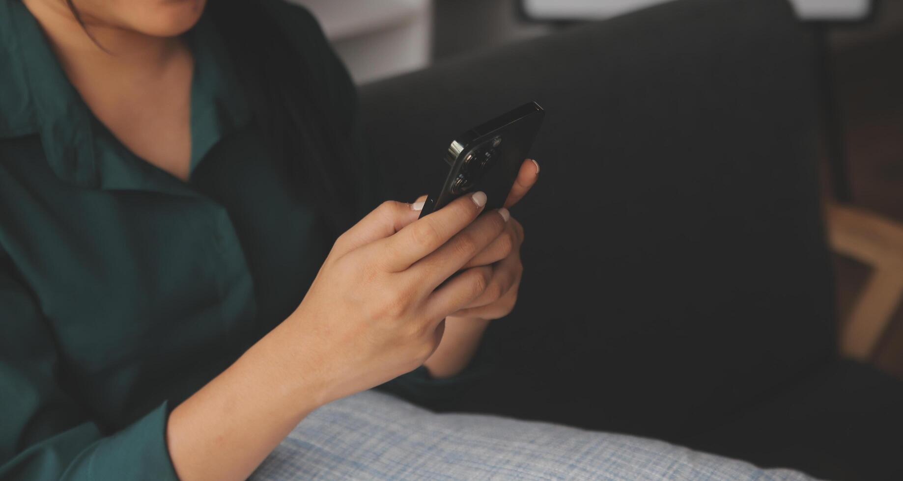 Charming young Asian woman using cellphone, communicating on web, working or learning online, sitting in armchair against white wall, free space. Lovely millennial lady chatting on smartphone photo