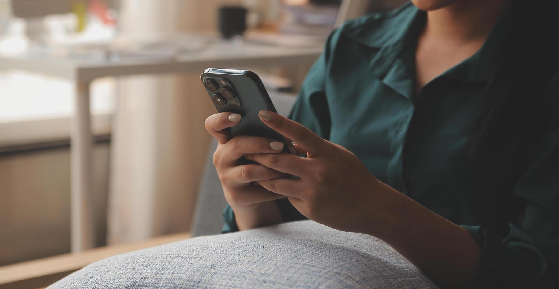 Charming young Asian woman using cellphone, communicating on web, working or learning online, sitting in armchair against white wall, free space. Lovely millennial lady chatting on smartphone photo