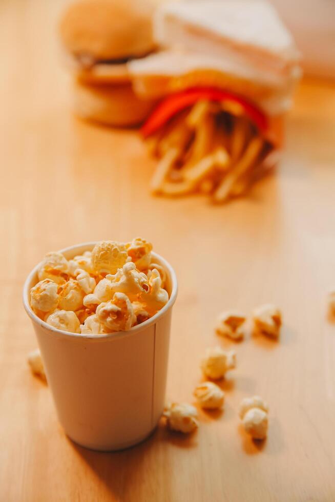 A bucket of popcorn, top-view, warm colors, light brown wooden background, flat lay, daylight macro close-up photo