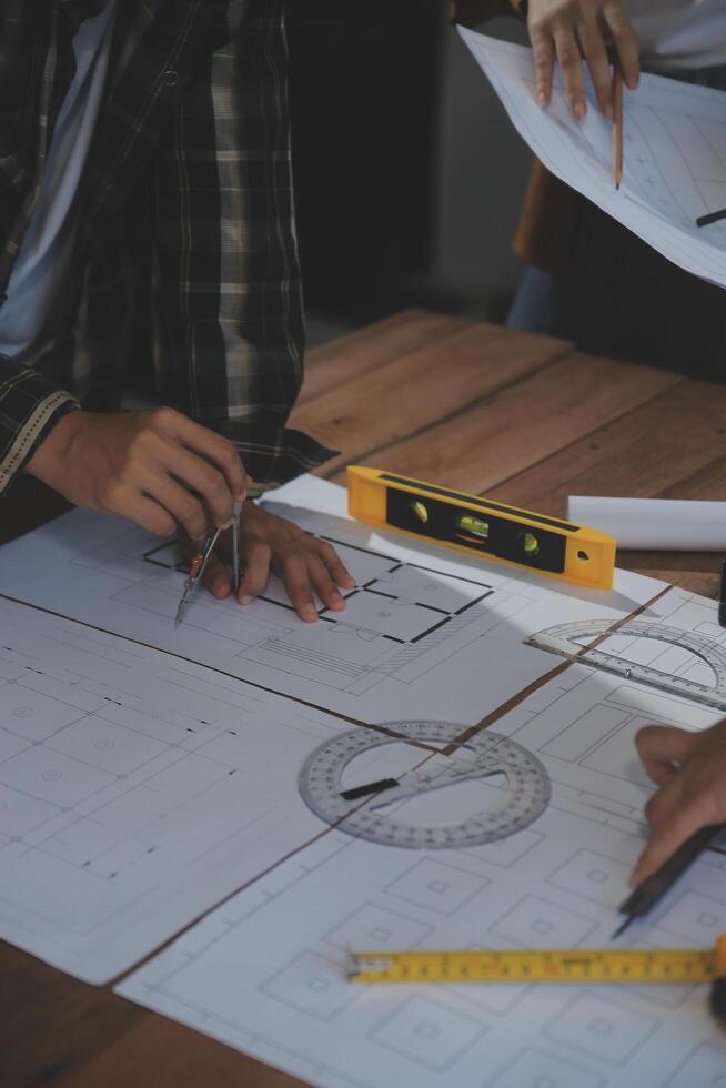 Team of multiethnic architects working on construction plans in meeting room. Engineers discussing on project in office. Mature businessman and woman standing around table working on blueprint. photo