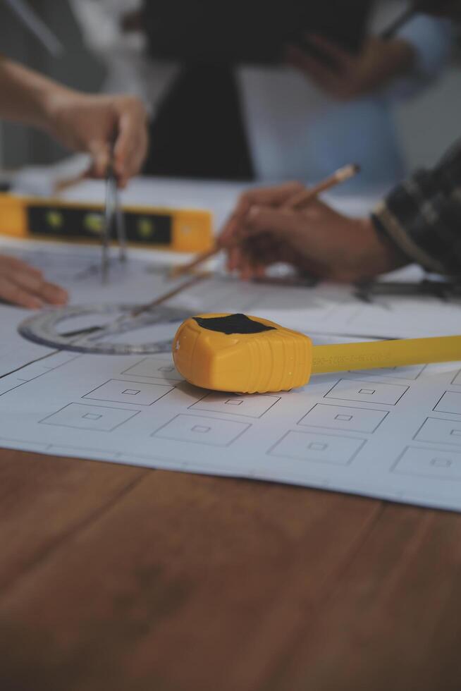 Team of multiethnic architects working on construction plans in meeting room. Engineers discussing on project in office. Mature businessman and woman standing around table working on blueprint. photo