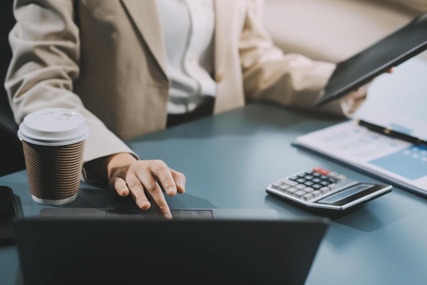 Asian Businesswoman Using laptop computer and working at office with calculator document on desk, doing planning analyzing the financial report, business plan investment, finance analysis concept. photo