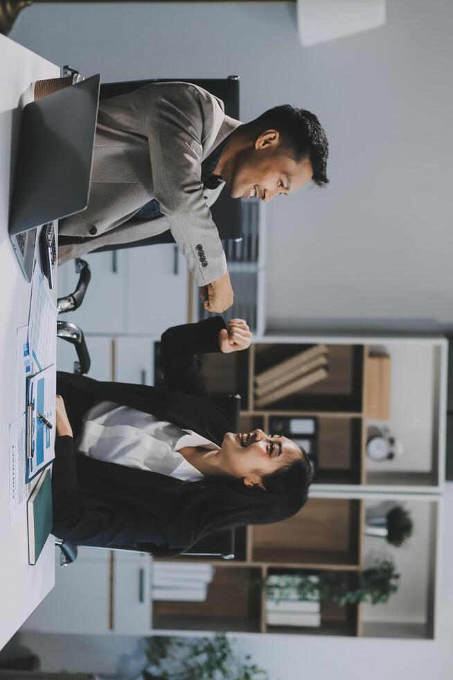 Young asian business woman giving high five with friends while working with computer laptop at office. photo