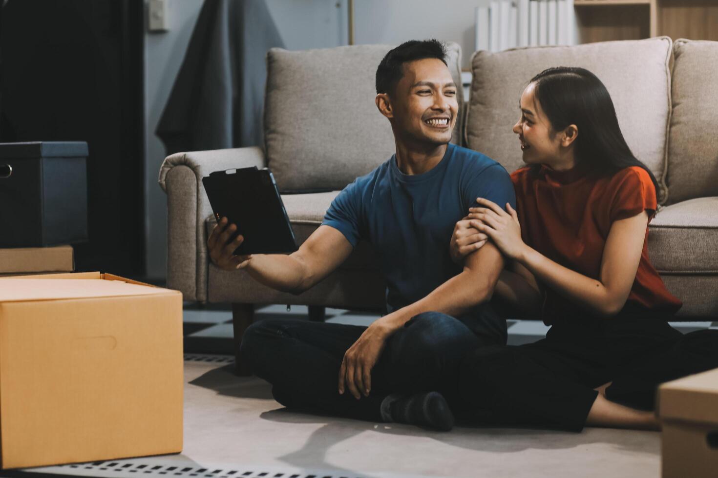 Happy excited, smiling asian young couple love using tablet pc, great deal or business success, received or getting cash back, tax refund, good news by mail while sitting on floor at home. photo