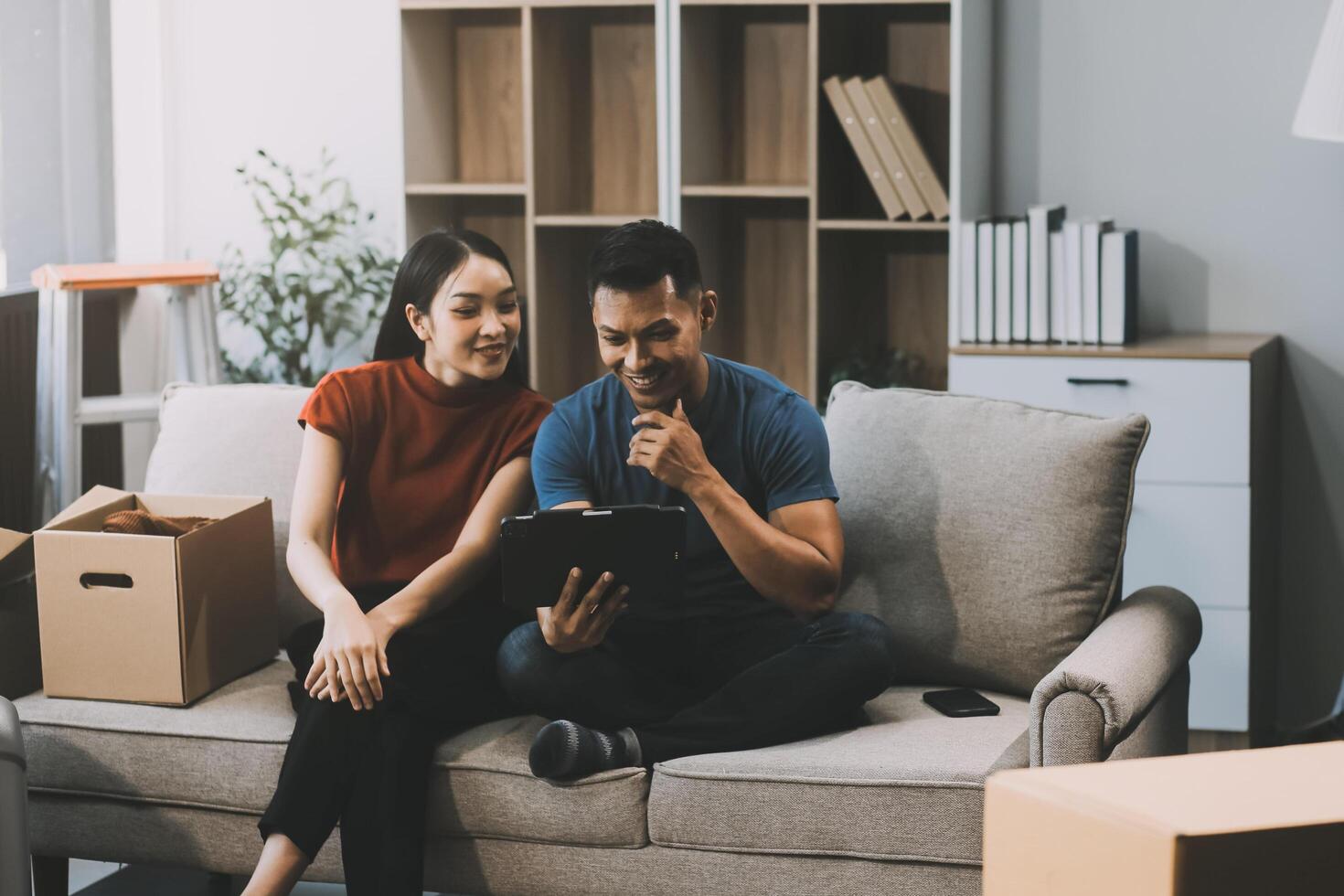 Happy excited, smiling asian young couple love using tablet pc, great deal or business success, received or getting cash back, tax refund, good news by mail while sitting on floor at home. photo