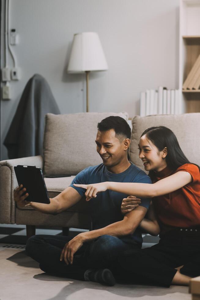 Happy excited, smiling asian young couple love using tablet pc, great deal or business success, received or getting cash back, tax refund, good news by mail while sitting on floor at home. photo
