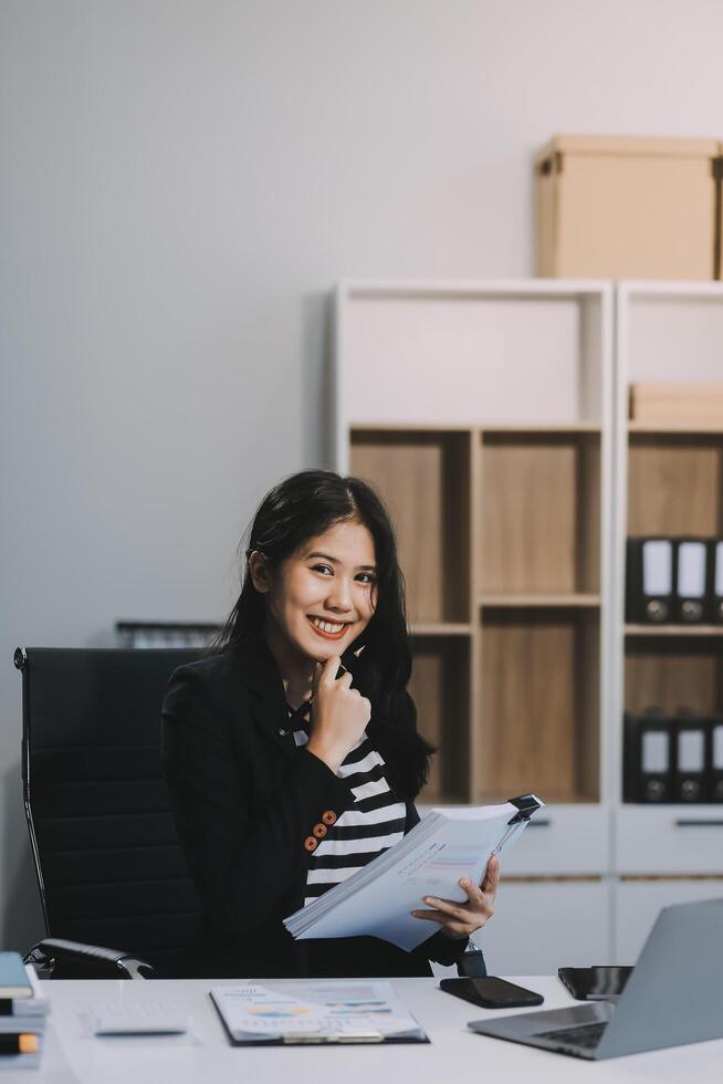 Charming Young asian businesswoman sitting on laptop computer in the office, making report calculating balance Internal Revenue Service checking document. photo