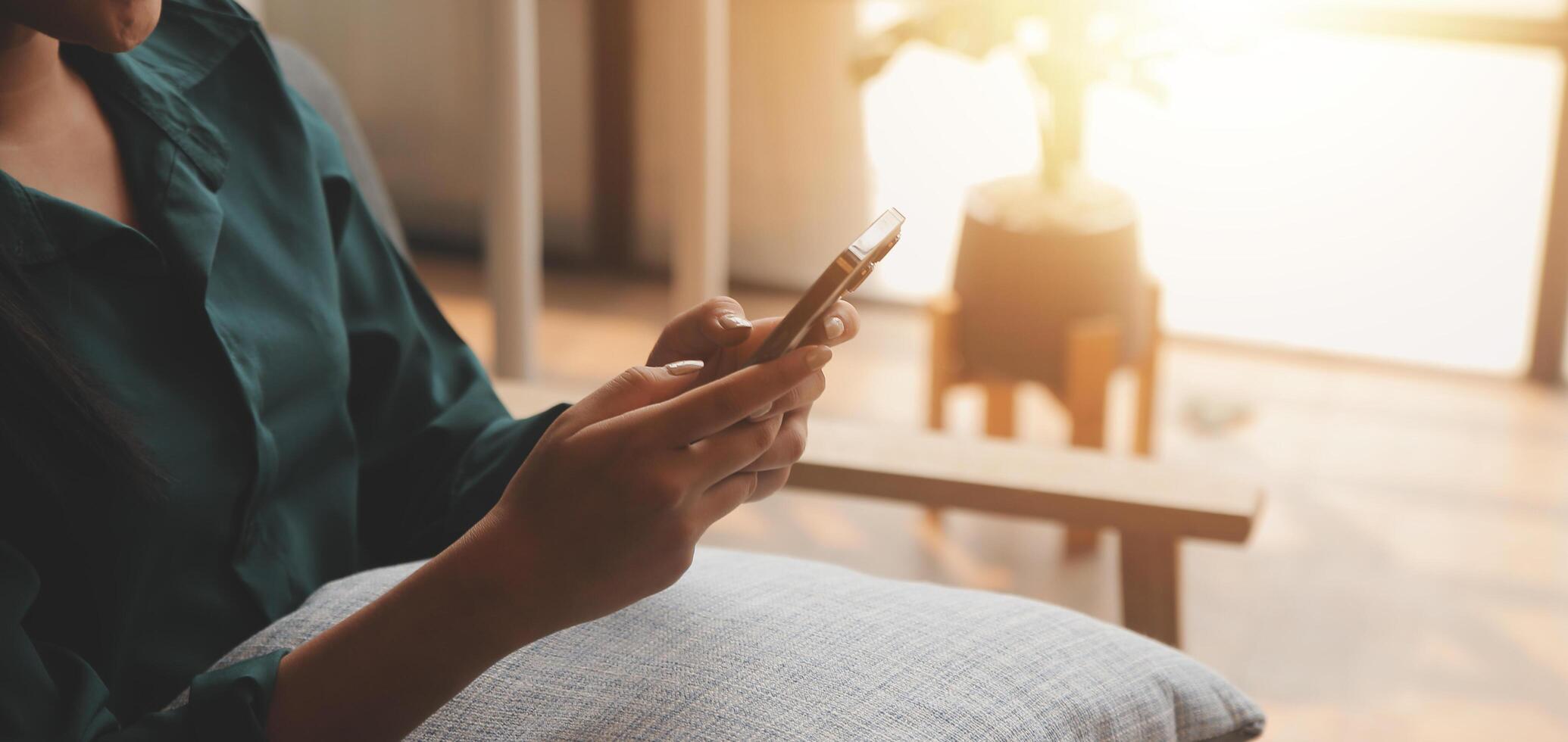 Charming young Asian woman using cellphone, communicating on web, working or learning online, sitting in armchair against white wall, free space. Lovely millennial lady chatting on smartphone photo