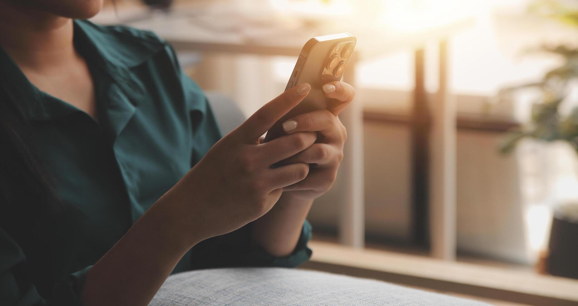 Charming young Asian woman using cellphone, communicating on web, working or learning online, sitting in armchair against white wall, free space. Lovely millennial lady chatting on smartphone photo