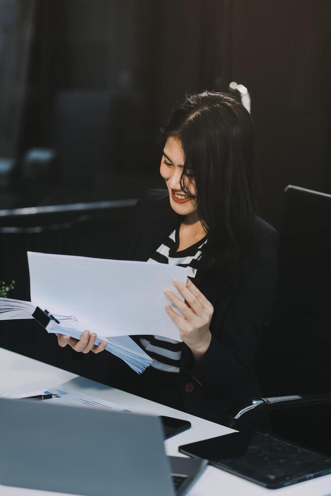 Charming Young asian businesswoman sitting on laptop computer in the office, making report calculating balance Internal Revenue Service checking document. photo