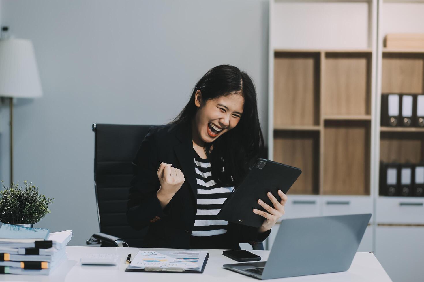 Asian business woman are delighted and happy with the work they do on their tablet, laptop and taking notes at office. photo
