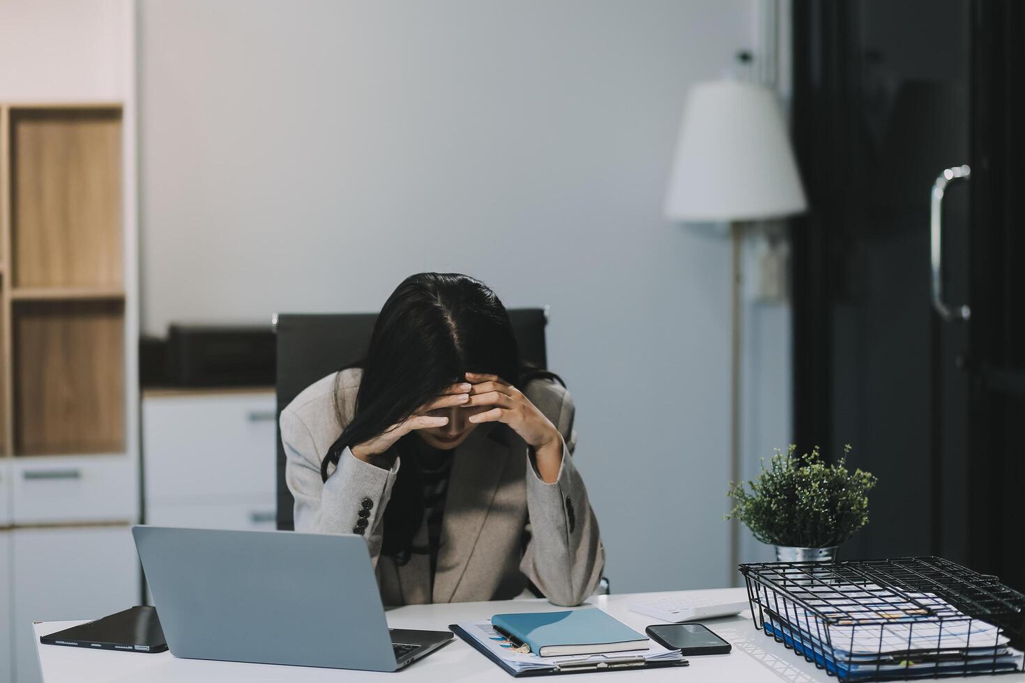 Young Asian woman feeling migraine head strain. Tired, Overworked businesswoman financier while working on laptop computer in office. photo