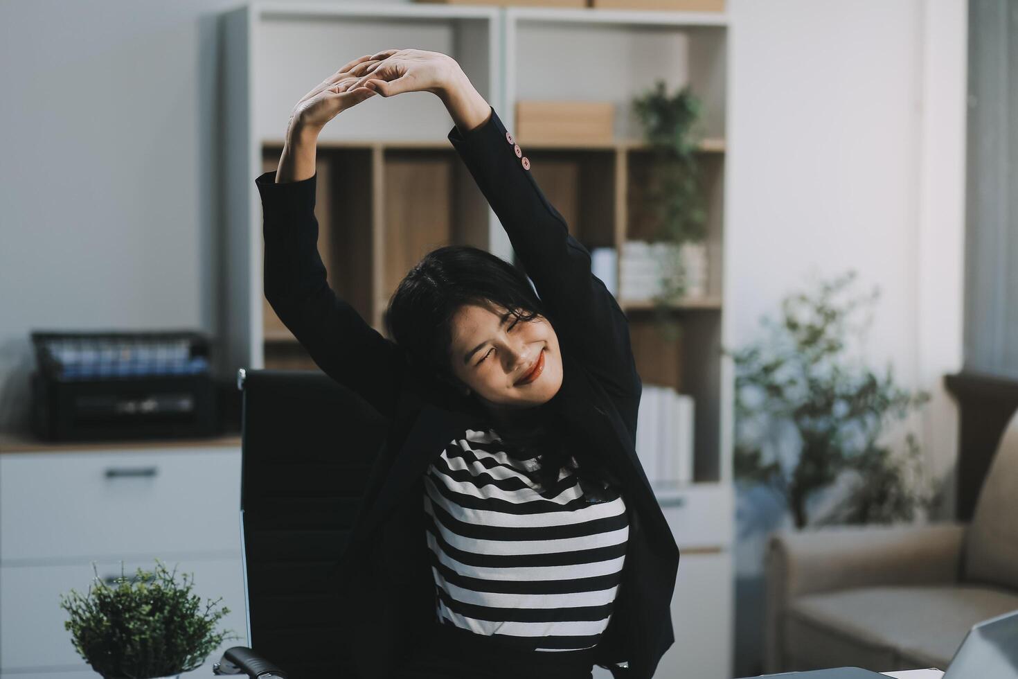 Office asian business woman stretching body for relaxing while working with laptop computer at her desk, office lifestyle, business situation photo