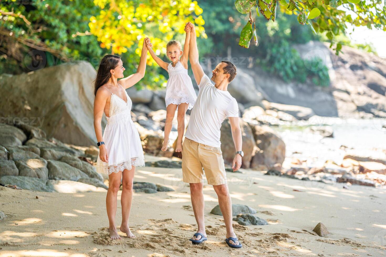 Happy young family of three taking a walk on the beach, having a fun on seashore in the shade of trees and palms. Happy family concept. High quality photo