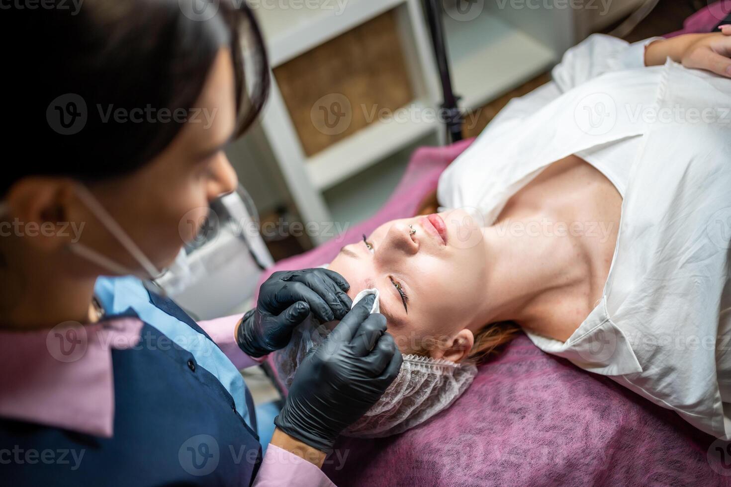 Permanent makeup artist prepares the client's face with the procedure, cleans the eyebrows from dirt and grease with a cotton pad. Eyebrow permanent makeup procedure, microblading. High quality photo