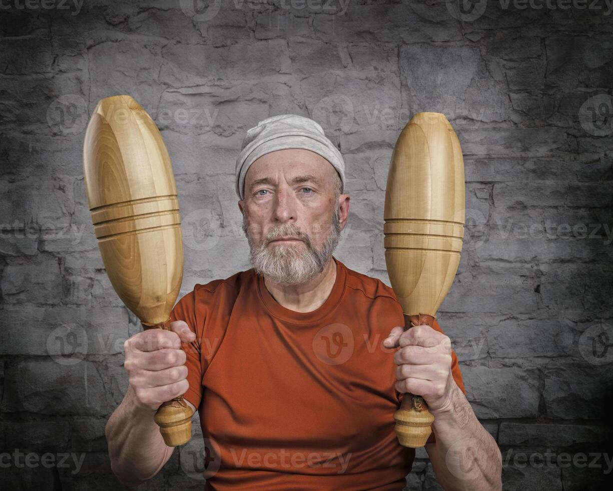 senior man is exercising with wooden Indian clubs photo