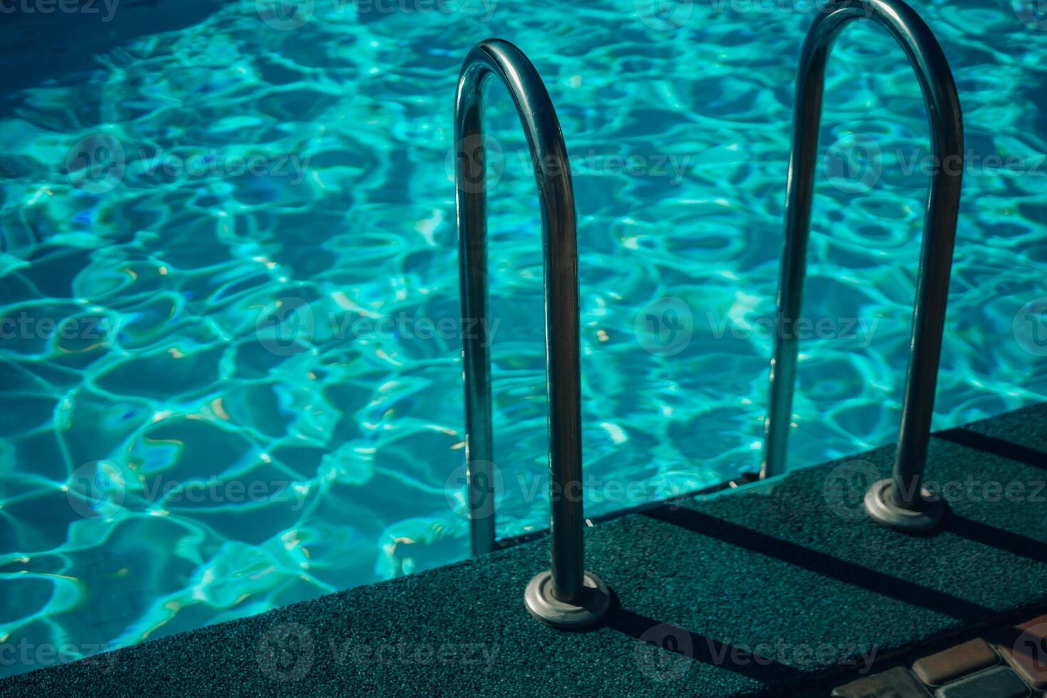 A metal ladder is in the water. The water is clear and calm. The ladder is in the middle of the pool. photo