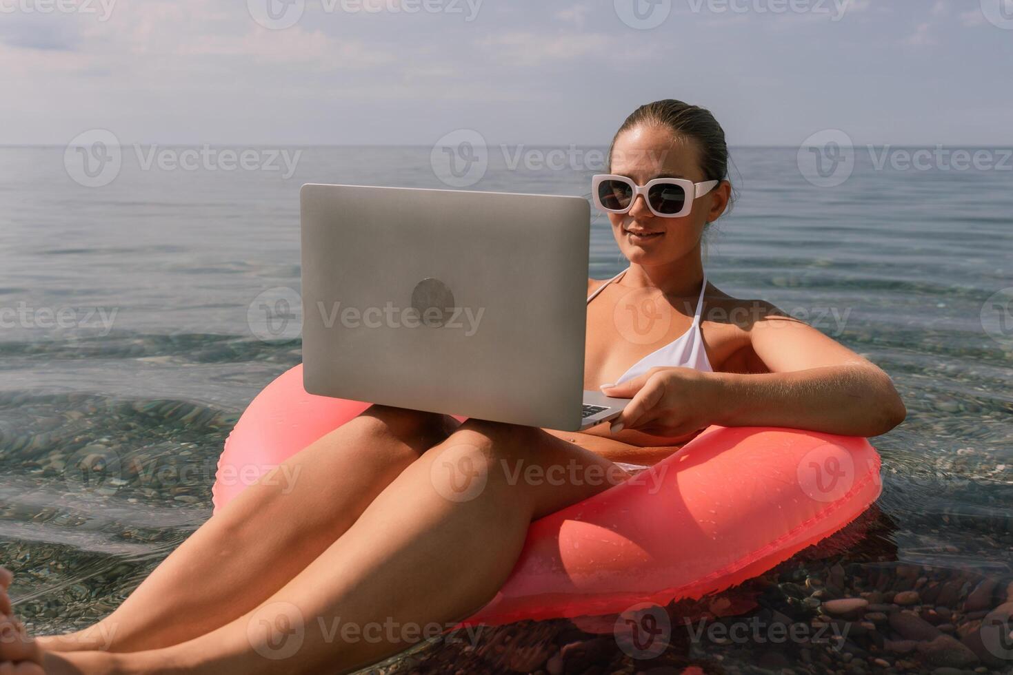 A woman is sitting on a pink inflatable raft with a laptop on her lap photo