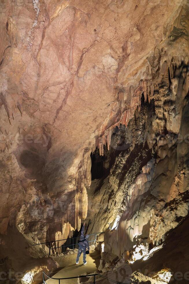 A man is walking through a cave with a large rock ceiling. The cave is dark and the man is holding a flashlight. photo