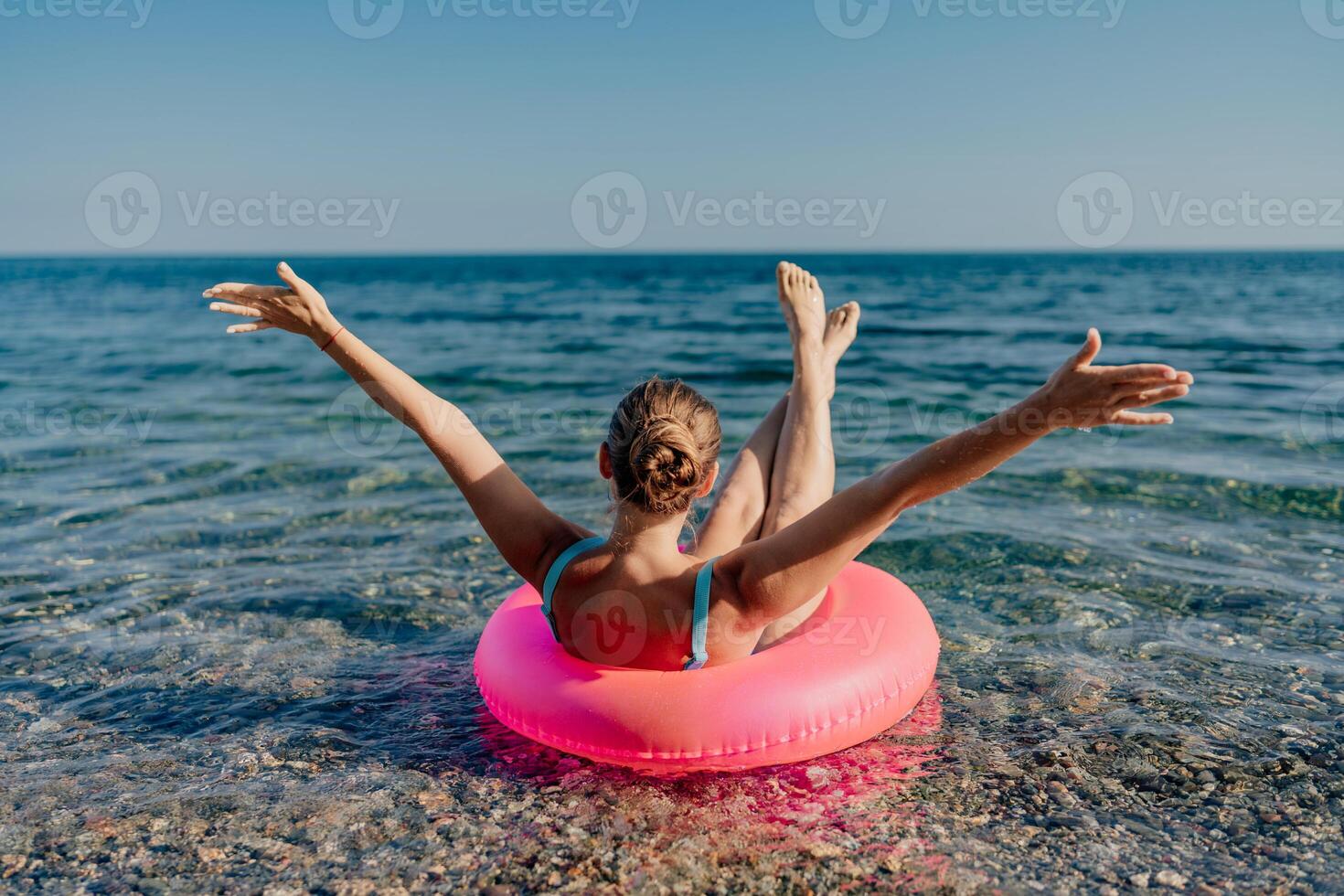 A woman is floating in a pink inflatable raft on a beach photo