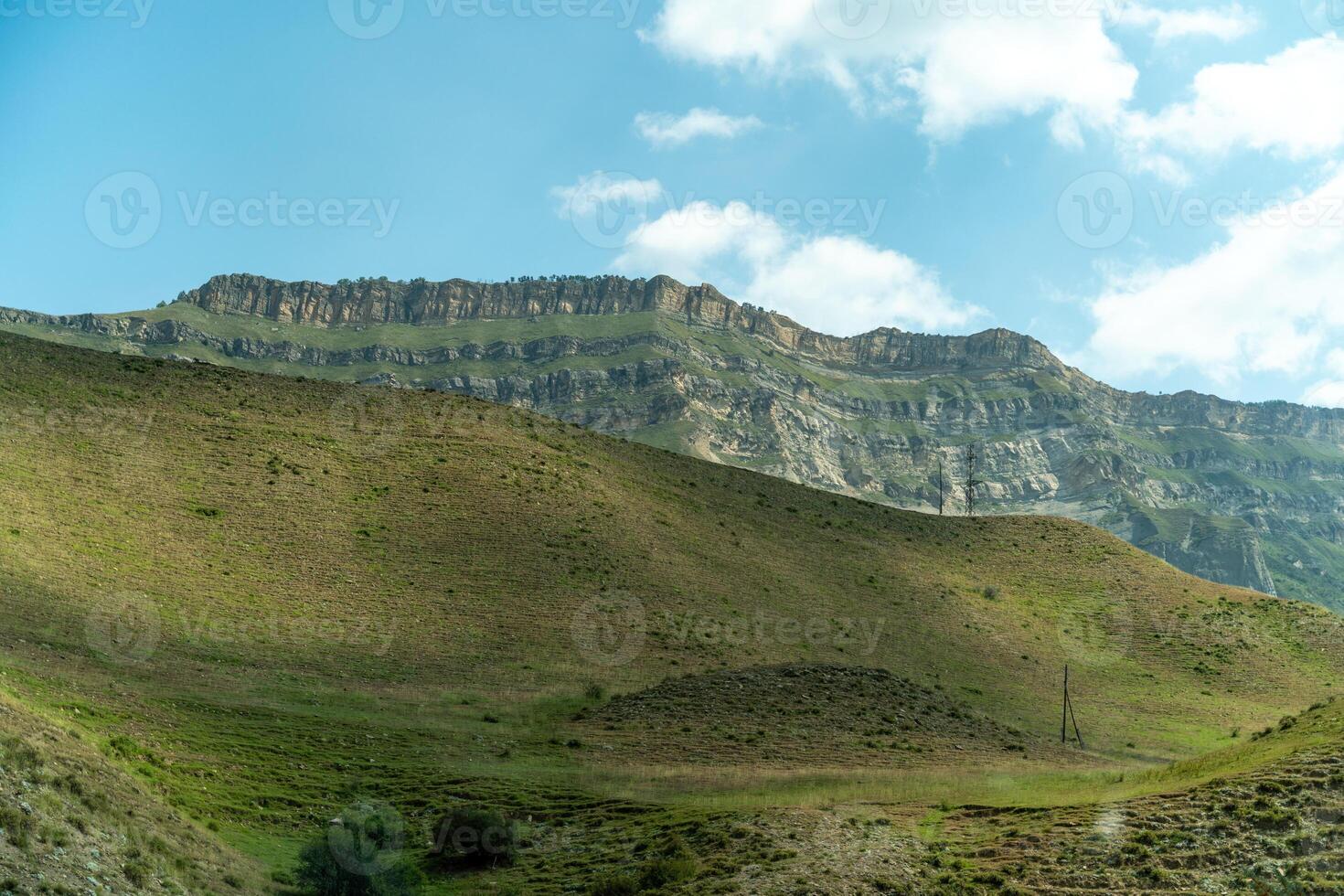 A mountain range with a green hillside. The sky is clear and blue. The mountain range is covered in grass and rocks. photo