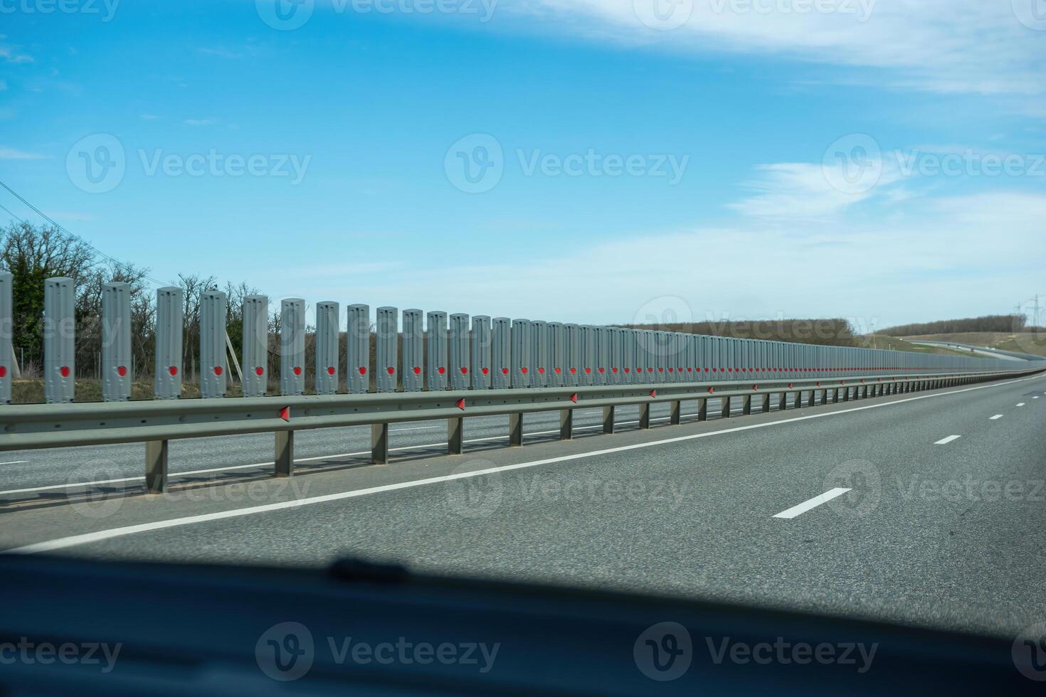 A road with a long line of metal posts with red hearts on them. The road is empty and the sky is clear. photo