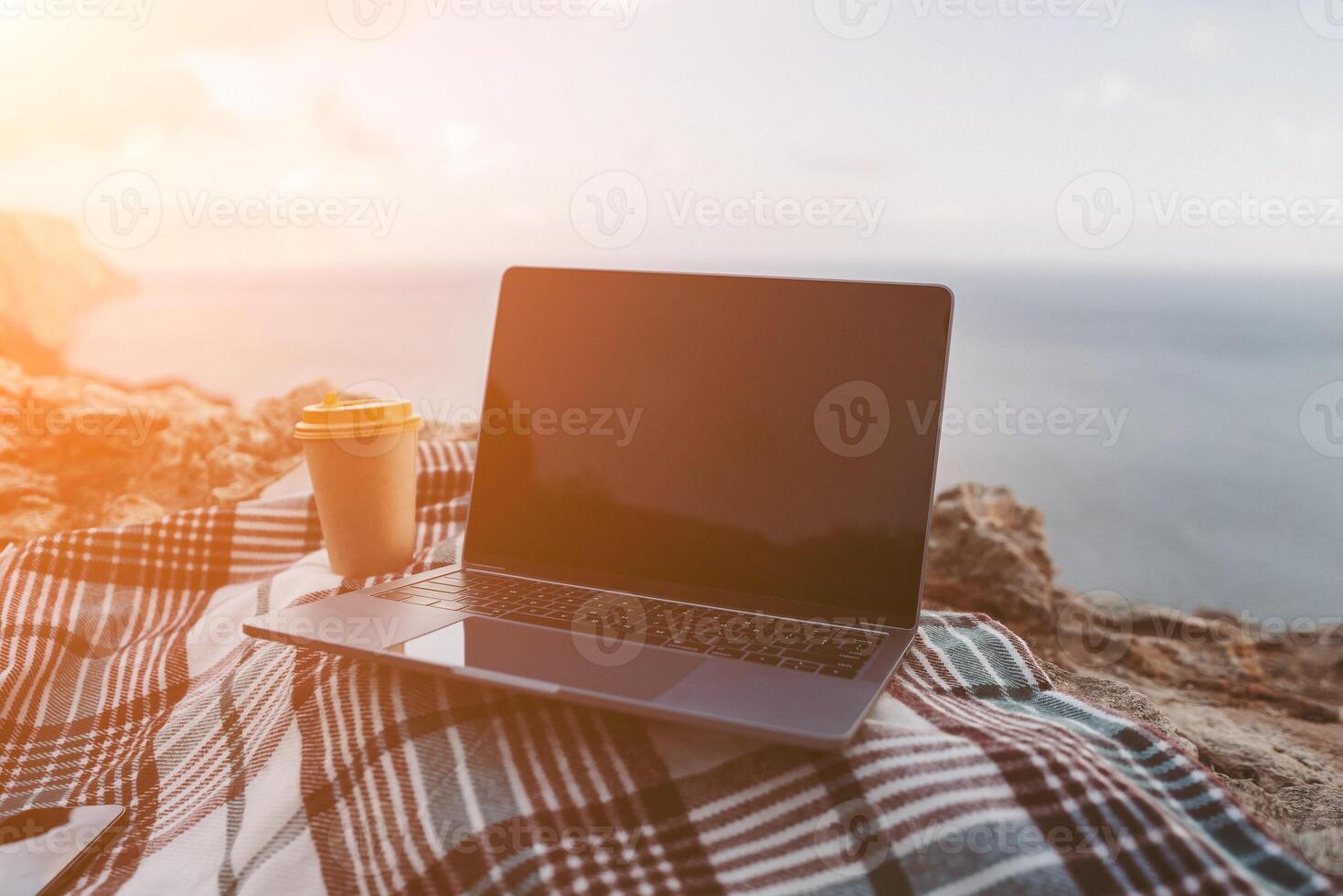 Laptop coffee on blanket with ocean view. Illustrating serene outdoor laptop use. Freelancer enjoying their time outdoors while working or browsing the internet. photo