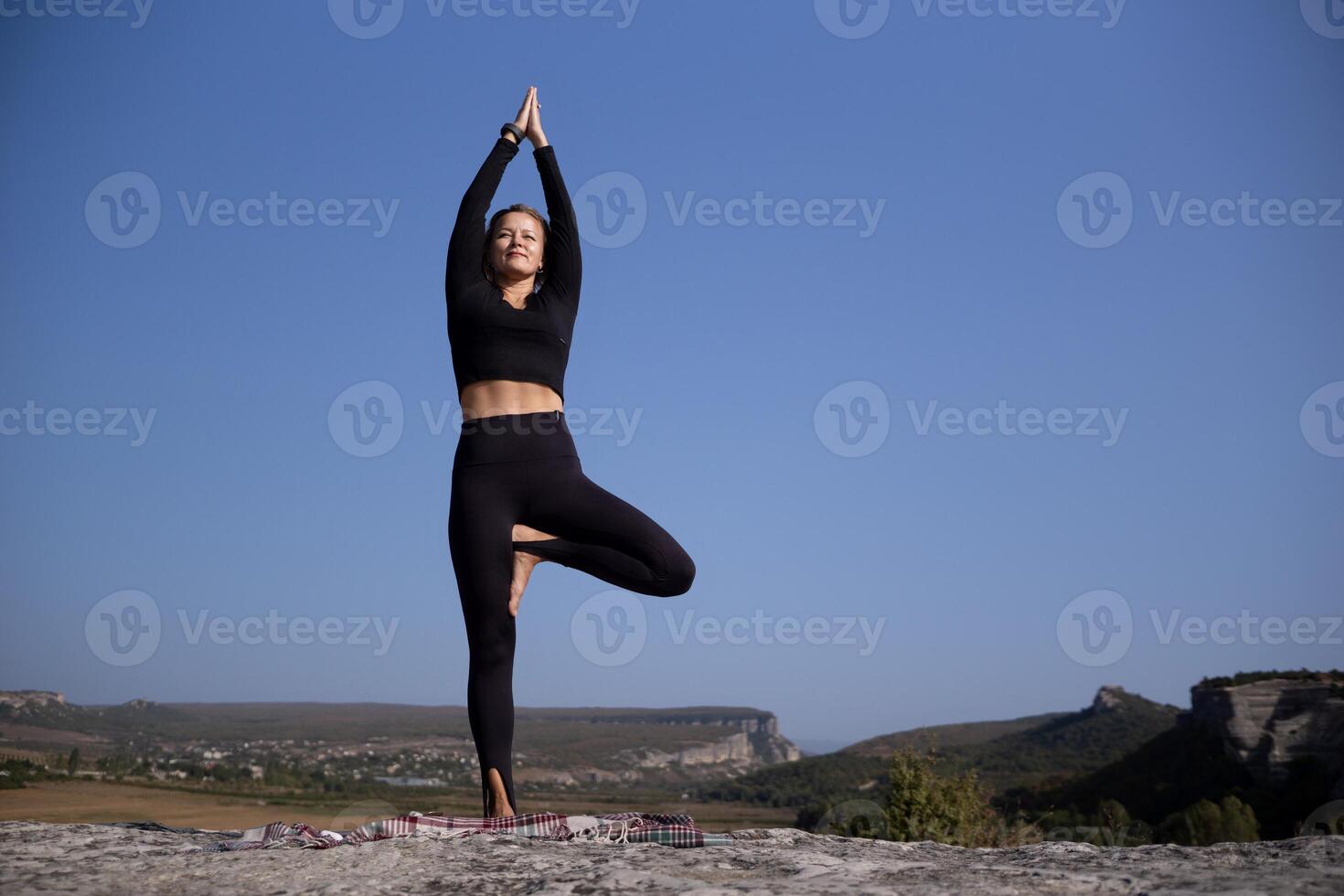 A woman is doing yoga on a rock in a beautiful mountain setting photo